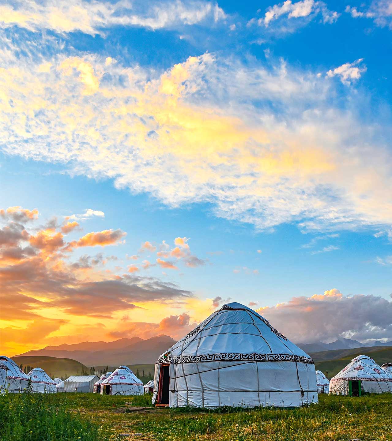 Jurtenlager auf Wiese vor Bergen bei Abendrot.