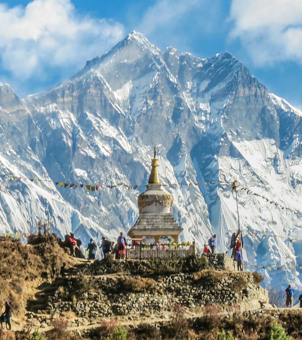 Stupa mit Gebetsfahnen, Menschen vor hohen Schneegipfeln.