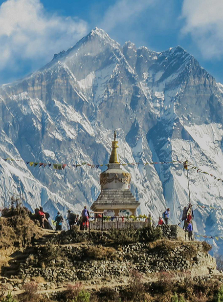 Stupa und Menschen vor schneebedeckten Bergen.