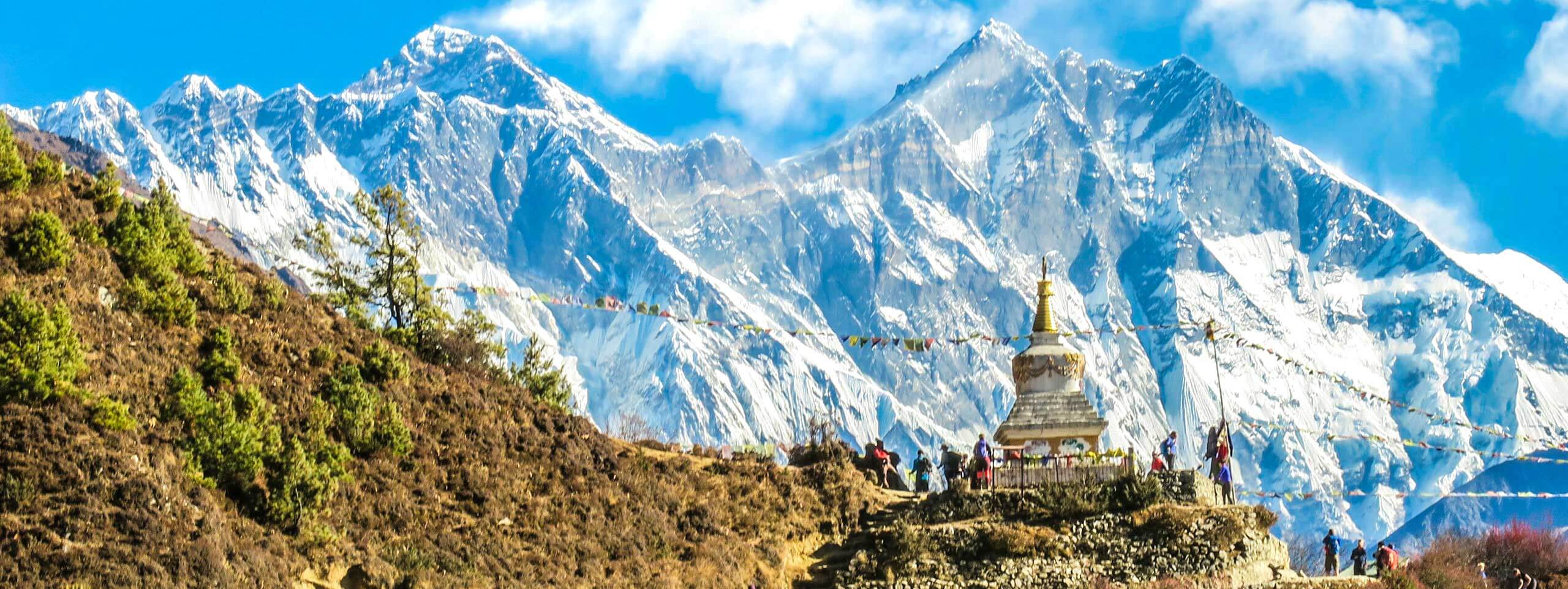 Stupa und Gebetsfahnen vor schneebedeckten Bergen.
