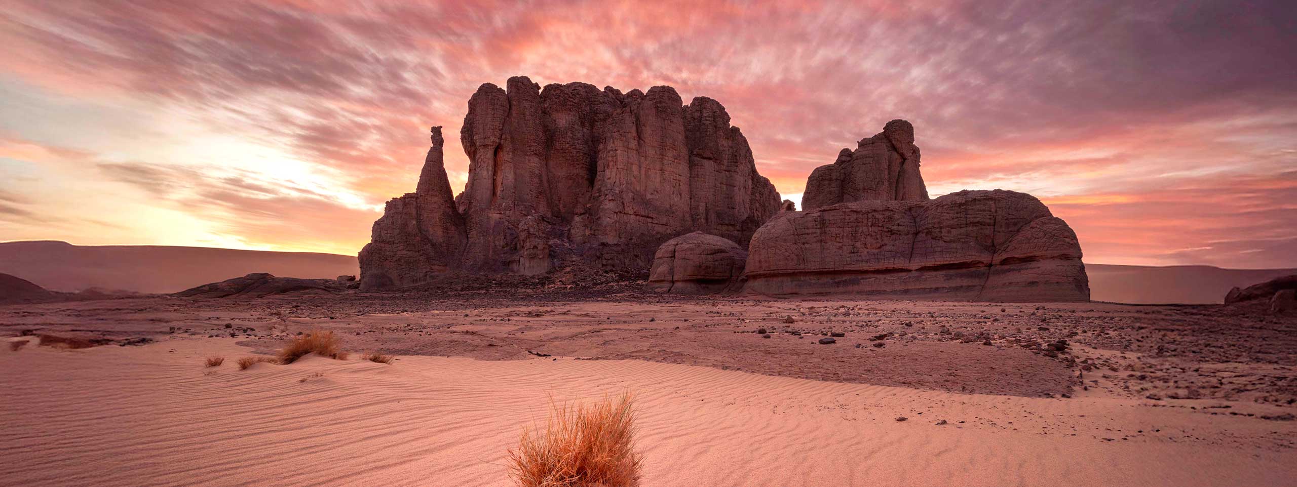 Wüstenlandschaft mit Felsen und rosa Himmel bei Sonnenuntergang.