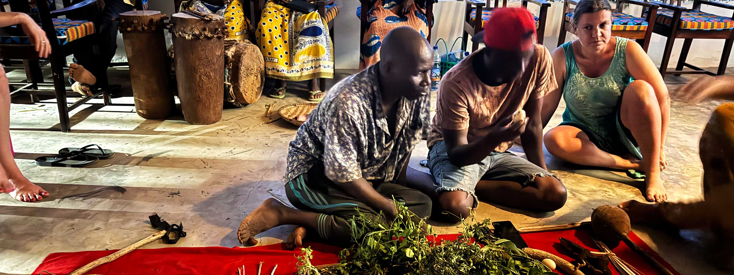 Drei Menschen sitzen auf dem Boden vor Kräutern und Trommeln.