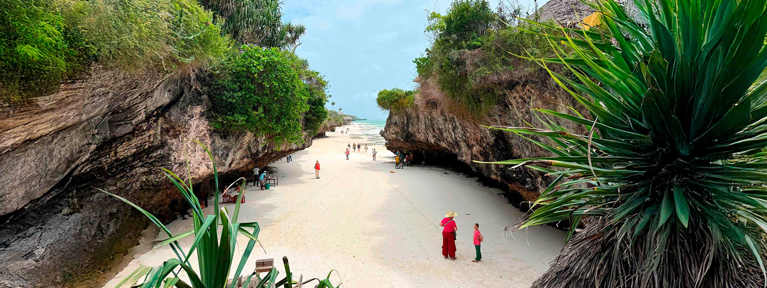 Sandstrand zwischen felsigen Klippen mit Vegetation und Menschen.