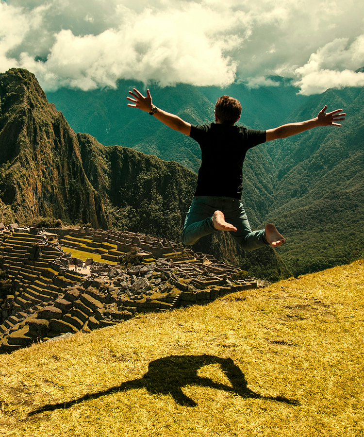 Person springt mit ausgebreiteten Armen über Machu Picchu.
